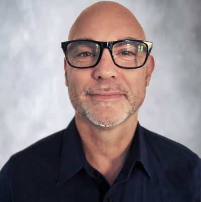 Pete Brown, senior executive testimonial headshot, wearing dark glasses and navy shirt against neutral grey background.